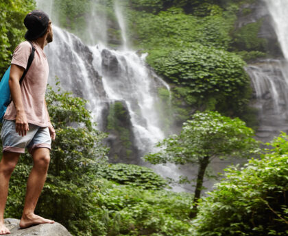 Man standing in front of a scenic waterfall showcasing eco-tourism in Kerala.