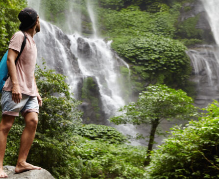Man standing in front of a scenic waterfall showcasing eco-tourism in Kerala.